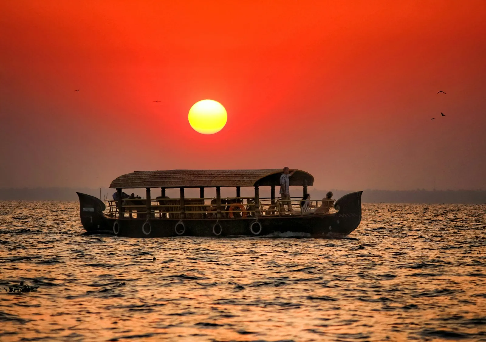 A thatched Kerala houseboat silhouetted against a fiery sunset on the backwaters