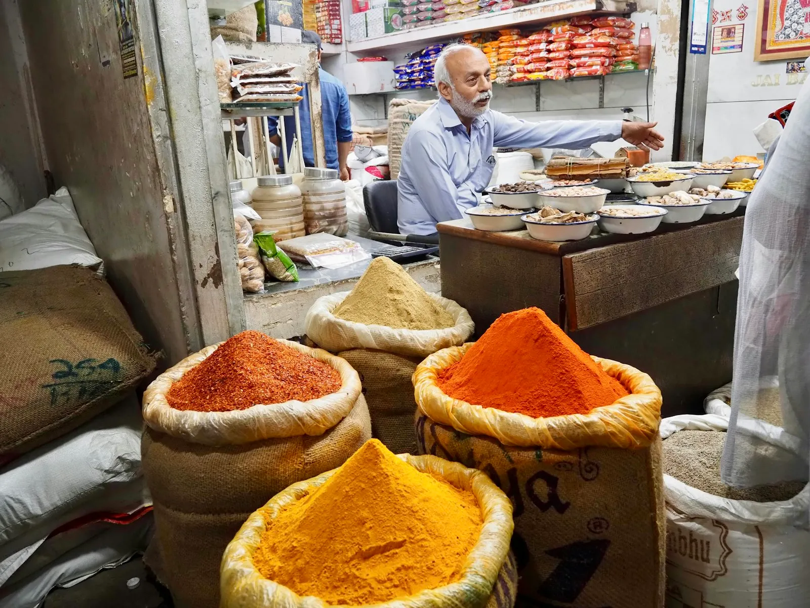 A vendor at a Delhi spice market behind open bins of turmeric, chilli and masala powders