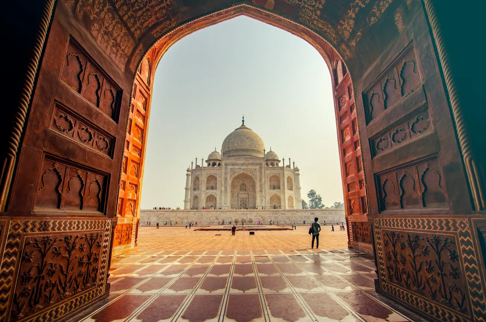 A traveller with a backpack framed by the red sandstone gateway leading to the Taj Mahal